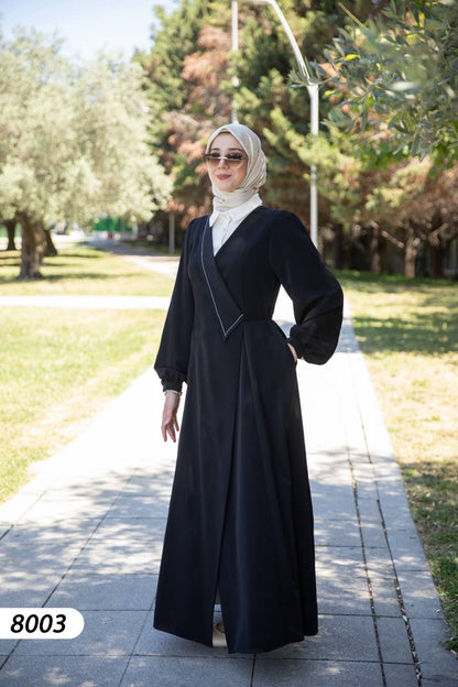 alwaan black maxi abaya dress with white collared shirt insert, wrap bodice, and long sleeves worn by a woman outdoors