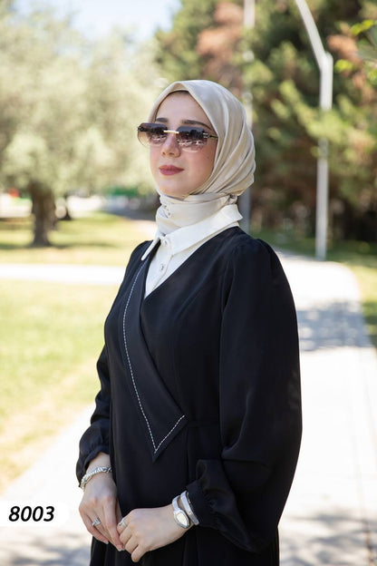 alwaan black wrap-style abaya dress with white collar and layered shirt detail worn with a beige hijab outdoors