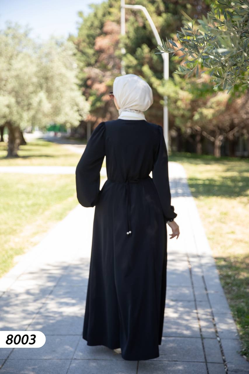 alwaan black maxi abaya dress with white collar, long sleeves, and adjustable back tie worn by a woman in a park